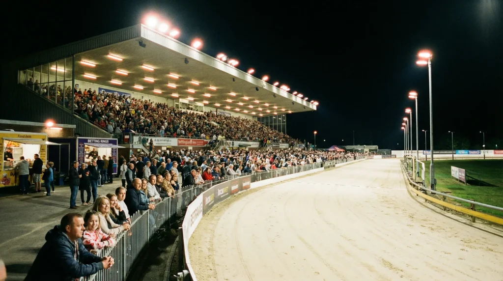Towcester greyhound stadium packed with spectators on a Saturday evening under bright floodlights